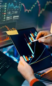 A person analyzing stock market data on a tablet using a stylus, with charts in the background, capturing finance, growth, and investment strategy concepts
