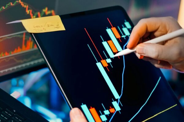 A person analyzing stock market data on a tablet using a stylus, with charts in the background, capturing finance, growth, and investment strategy concepts