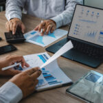 Business team reviewing accounting financial reports with calculator, charts, tablet, and dashboard on laptop during office meeting, supporting budget analysis, financial planning, and reporting workflow.