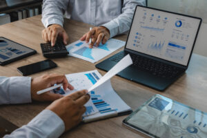 Business team reviewing accounting financial reports with calculator, charts, tablet, and dashboard on laptop during office meeting, supporting budget analysis, financial planning, and reporting workflow.