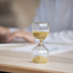 Unknown businesswoman working on laptop, focus on hourglass on desk