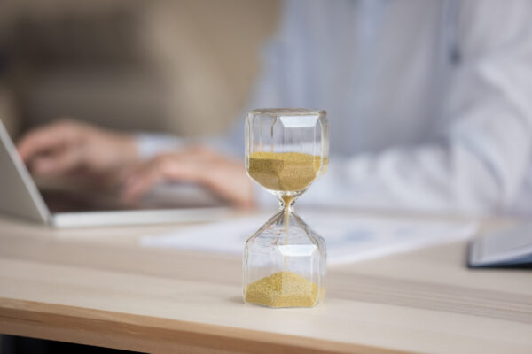 Unknown businesswoman working on laptop, focus on hourglass on desk